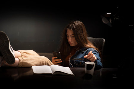 Female student sitting with her feet on a desk and a message key on a mobile phoneの写真素材