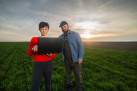 A woman agronomist and a young farmer examine planted young wheat in the springの写真素材