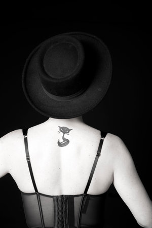 Young woman in black hat on black background from back. Black and whiteの写真素材