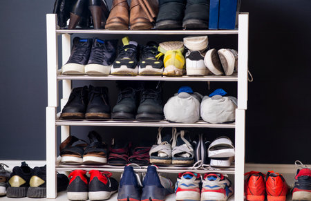 A collection of different shoes and sneakers of one family in a shoe rack. Wardrobe with shelves in...