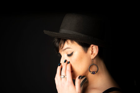 Profile of a young and beautiful woman with black short hair wearing a black hat on a black...