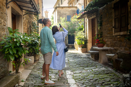 A couple walks around a small medieval town in the Mediterranean country and takes photos with their phone. A clear and sunny day. Istrian Peninsula, Croatiaの写真素材