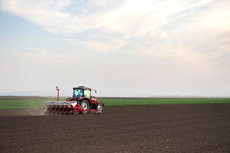 Farmer with tractor seeding - sowing crops at agricultural fields in springの写真素材