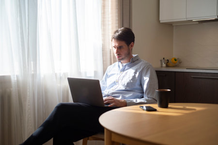 Young man working in a relaxed home atmosphere, using a laptop computer. Remote work, connection, self-employed, freelancer lifestyle conceptの写真素材