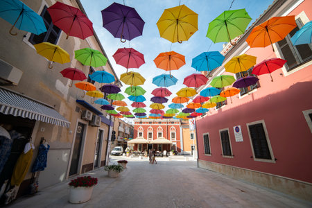 A street with umbrellas in a Mediterranean country. Beautiful window shutters. Clear and sunny day. 17.06.2025. Novigrad, Istrian Peninsula, Croatiaの写真素材