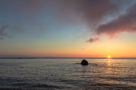 Sunset over the sea with a silhouette of a rock in the foreground. Bird's Cape at sunrise, South Sakhalin, Russiaの写真素材