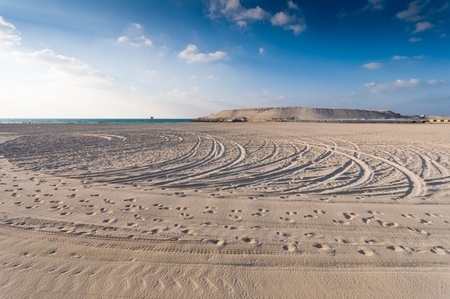 sandy beach with lots of footprints and a blue sky with cloudsの写真素材