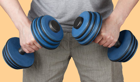 A man holds dumbbells in two hands and strains muscles to lift them. The plot close-up on a yellow...