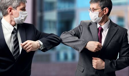Two businessmen with a medical mask on their faces greet in a new way, striking with their elbows instead of a handshake. Social distance during the coronavirus epidemicの写真素材