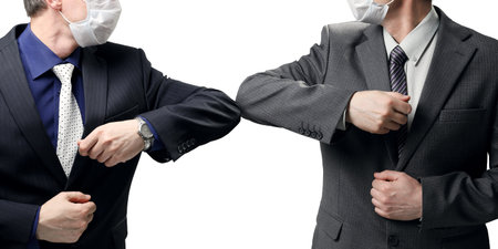 Two businessmen in suits greet each other without a handshake due to the danger of infection