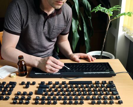Man stays at home and thorough cleans the disassembled keyboard. Alcohol disinfection of the surface and insideの写真素材