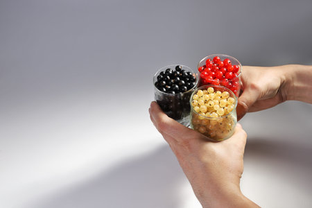 Hands clasp and hold together three glasses with berries of different colors. Delicious food from...