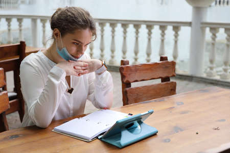 Young beautiful woman in a white blouse sitting at the table outdoors. She got distracted from working with papers and a tablet and thought about somethingの写真素材
