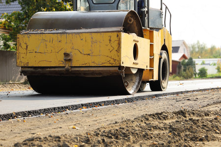 Heavy road roller is rolling and compacting new flat asphalt on deserted street in provincial town