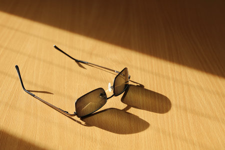 Glasses with dark lenses on wooden table with their shadow, close-up with copy space