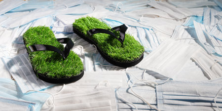 Green slippers, with imitation grass on the surface of disposable medical masks that pollute the planet. Concept of environmental problemsの写真素材