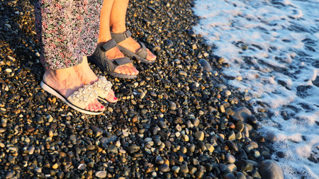 Legs of couple in sandals stand side by side on the pebbled seashore at sunset. Relationship and friendship conceptの写真素材