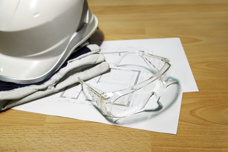 Selective focus on protective construction goggles in composition with white helmet and blueprints on the surface, close-upの写真素材
