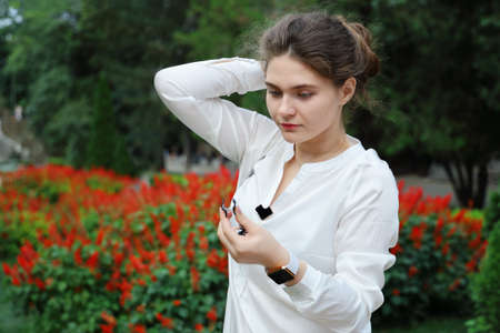 Young woman in white blouse wants to fix hairstyle on head, summer day in park close-upの写真素材
