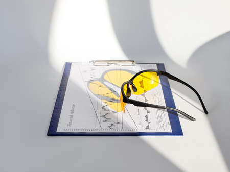 Yellow glasses on financial diagram on white surface with gray shadows close-up without peopleの写真素材