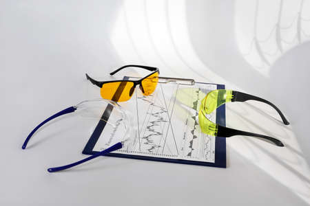 Glasses of different colors are on financial graph on white surface close-up. Concept business meeting between ethnic diversityの写真素材