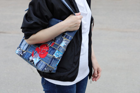 Part of body of woman, which carries bag made of denim tissue on her shoulder, close-up