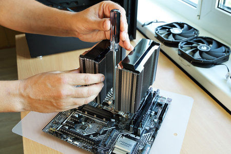 St. Petersburg, Russia - July 17, 2021: Assembling new computer, hands screw powerful cooling cooler with screwdriver to modern processor on Asus motherboardのeditorial素材