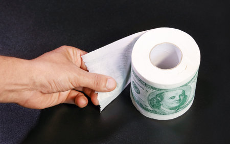 Roll of toilet paper in form of dollars, hand holds unlocked edge. Concept of deficit and high cost...