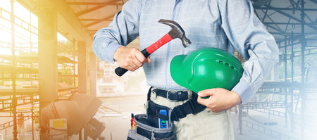 Hard hat and hammer in hands of builder, safety concept, protection when working in construction and...