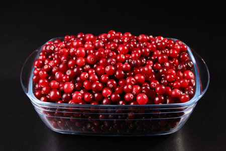 Glass bowl with cranberries on black background close-up