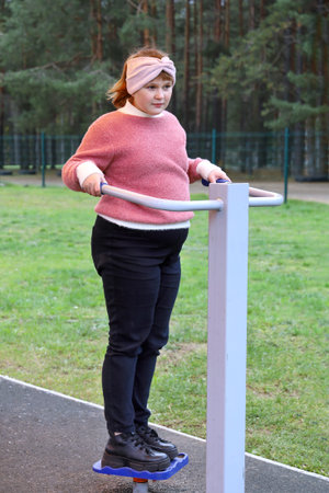 Chubby girl performs sports exercises on street simulators outdoors
