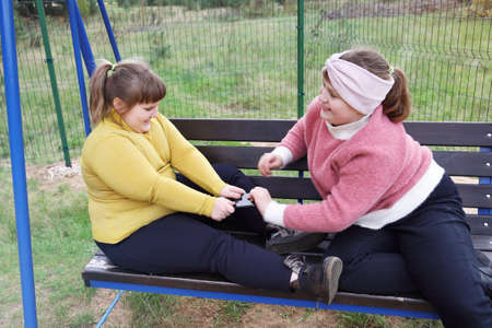 Quarrel two girls because of smartphone, take away gadget from each other, on outdoor benchの写真素材