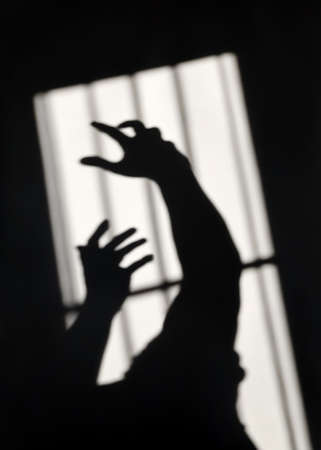 Soft focus, dark shadow on wall, concept hands behind prison fence seek to freedomの写真素材