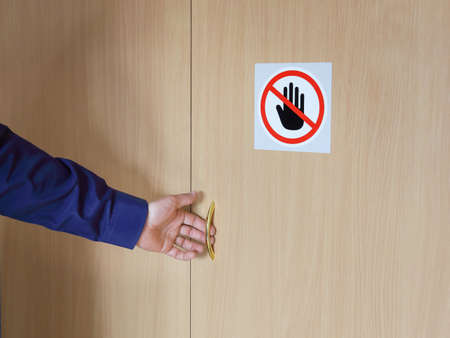 Hand of person opens door on which warning sign of ban, stop handの写真素材