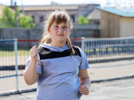 Chubby girl in sportswear runs in for sports, close-up portrait on sunny summer day