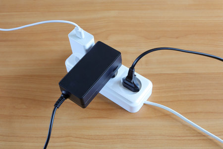 Different devices plugs are connected to multiple outlets of energy on wooden surface, close-up