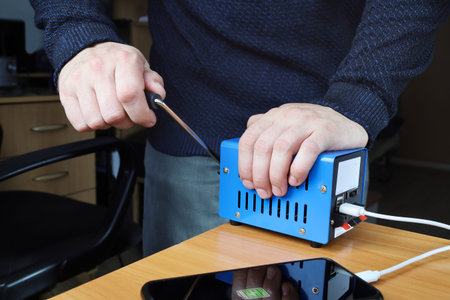 Human hands rotate handle of electricity generator, charge smartphone, charge level on screen, for emergency situation when there is no electricityの写真素材