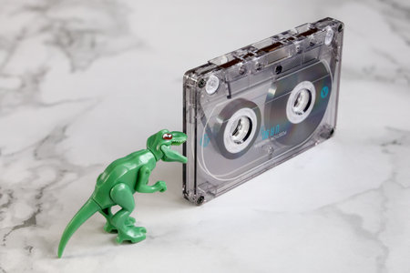 Extinct audio cassette, outdated technology, small green dynazaur looks, opening his mouth, close-upの写真素材