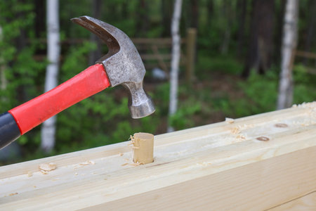 hammer strikes wood dowel to secure connection of wall timbers, building a new wooden house