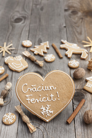 Heart shaped Christmas gingerbread with white icing,  on wooden background, written in Romanianの写真素材