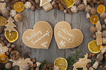 Two heart shaped gingerbreads with white icing, on wooden background, with Merry Christmas written in Hungarian and Romanianの写真素材