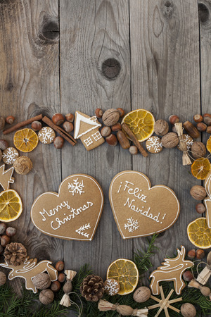 Two heart shaped gingerbreads with white icing, on wooden background, with Merry Christmas written in English and Spanishの写真素材