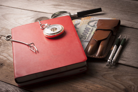 Retro clock , Notobook, magnifying glass, money, pen and pen case an a wooden tableの写真素材