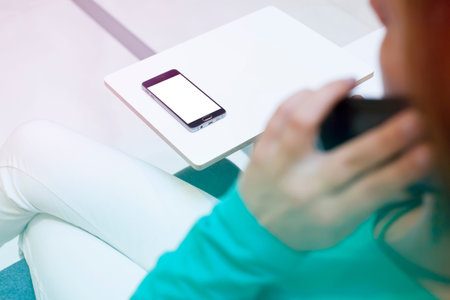 Contemporary modern smartphone on a desk in front of woman phoning. Visual effects. Blank display...