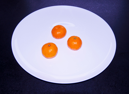 three tasty tangerines on a white plateの写真素材