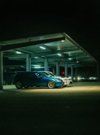 A Tranquil Night Scene Featuring a Blue Car and Other Vehicles Under a Sheltered Parking Area Illuminated by Soft Lights