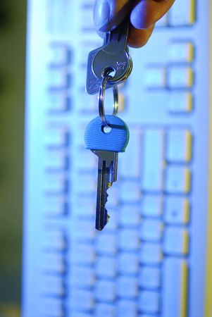 A hand holding keys in front of a keyboardの写真素材