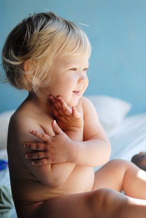 A little laughing blonde girl sitting on bedの写真素材