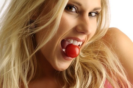 Blond girl with tomato on pink backgroundの写真素材