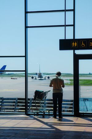 The man with luggage staying before the window with view for aerportの写真素材